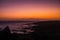 Romantic scenic sunset on the coast with black. rock beach and quiet wave ocean - sky and clouds in background - red and orange