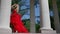 romantic shot of young blonde woman in red gown with rose posing between white columns