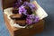 Romantic still life with lilac flowers and brownie, wet cake. Dessert for served with tea or coffee break in wooden box. Snack on