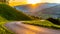 Romantic sunset in the mountains. Alpine rural curvy road, green meadows and high peaks of Austrian Alps. Pinzgau