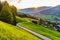 Romantic sunset in the mountains. Alpine rural curvy road, green meadows and high peaks of Austrian Alps. Pinzgau