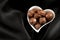Romantic sweet gifts for Valentines Day concept with a heart shaped bowl filled with chocolate pralines on black silk or satin