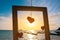 Romantic symbol of hearts in the wooden  frame at the sea background.Red heart model at the sandy sea beach with blue sea blurred