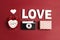 Romantic top down composition of the word love, alarm clock, vintage camera, gift and heart on red background