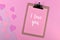 Romantic Valentine`s Day flatlay with clipboard with text `I love you` and paper hearts on pink background