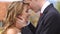 Romantic wedding portrait. The handsome groom is softly kissing his charming smiling bride in the head outdoor.