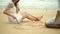 Romantic young couple draw heart shapes in the sand on the beach.