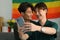 Romantic young gay couple taking a selfie with smartphone in living room rainbow flag in background. LGBT and love