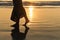 Romantic young girl walks on the beach barefoot in the water. Woman stroll barefoot in the sea at sunset.