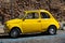 Rome, Italy - June 30, 2019: Cute little yellow retro car Fiat with a small dent parked on street