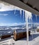 Roof with big sunlit icicles and small wooden houses at snowy winter mountains