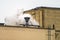 The roof of a brick building with metal structures and a cloud of steam.