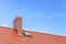 Roof with ceramic tile chimney against blue sky.