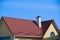 Roof and chimney of small house - red profile roofing sheets steel, yellow siding wall and blue sky