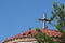 A roof with a cross on it surrounded by pigeons and greenery under a blue sky