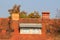 Roof windows surrounded with small roof tiles and red brick chimneys next to rusted metal pole with multiple connected electrical