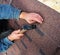 Roofer installs bitumen roof shingles - closeup on hands. Roofing repair