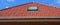 Roofing construction. A red tiled roof with a skylight window installed, a plastic rain gutter, a fascia board and a soffit