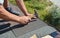 Roofing Construction. Roofer with hammer and nails laying asphalt shingles tiles on house roof