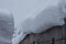 Roofs of houses with huge drifts of snow. In the background is a gray sky with large flakes of snow. The aftermath of