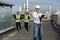 On the rooftop of construction site man engineer make a conversation with some worker using the tablet and ration