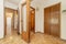 A room with built-in wooden wardrobes next to a corridor with a wooden and glass door and a checkerboard oak floor