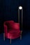 A room with a comfortable red velor armchair, a minimalist floor lamp in the living room with dark blue velvet wall panels and