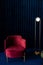 A room with a comfortable red velor armchair, a minimalist floor lamp in the living room with dark blue velvet wall panels and