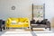 Room with yellow sofa, grey armchairs, shelf, clock and laptop in sunlight