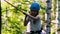 Rope adventure in the park - a little girl standing on the rope bridge in full insurance