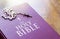 A rosary of white beads with a silver crucifix above the cover of the closed holy bible book. Religion and hope