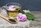 Rose herbal tea in a glass cup with pink petals and fresh flower on a rustic wooden table.Summer drinks.