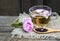 Rose herbal tea in a glass cup with pink petals and fresh flower on a rustic wooden table.Summer drinks.