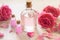 Rose oil in glass bottles with bright pink flowers on white wooden background