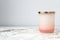 Rose pink and white ombre candle jar with a shiny gold lid, sitting on a bedside table night stand. Candle is not lit. Daytime