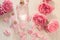 Rose water or oil in glass bottles with pink fresh rose flowers and petals on wooden background, SPA concept and aromatherapy