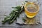 Rosemary herbal tea in a glass cup with fresh green rosemary herb on rustic wooden background.