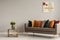 Roses in vase on wooden shelf with books next to comfortable sofa with orange, yellow, beige and emerald green pillows