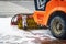 Rotating industrial brush of an orange tractor on a city street during a snowfall. Snow removal, brush machine in winter for