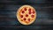 Rotating pepperoni pizzai on a wooden stand on a dark wooden background. Top view center orientation