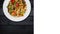 Rotating udon stir fry noodles with seafood and vegetables. In a white plate on black wooden background. Square layout