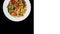 Rotating udon stir fry noodles with seafood and vegetables. In a white plate isolated on ablack background. Square