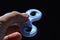 Rotating white fidget spinner toy held between thumb and index finger of adult male person, black background