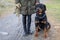 A rottweiler dog with a leash sits near a woman in a dog park in cold weather