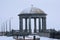 Rotunda on the embankment in winter. Snowing. The transparent dome is covered with snow. Granite columns, balustrade and