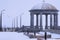 Rotunda on the embankment in winter. Snowing. The transparent dome is covered with snow. Granite columns, balustrade and