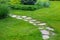 Rough different shapes of natural stone path paved in the green backyard turf lawn.