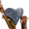 Rough figure of a heart made of gray pebble stone balancing on the stems of a rose with prickly thorns closeup