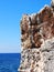 A rough jagged rocky outcrop against a bright blue sunlit sky and sea