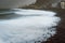 Rough ocean waves rolling foamy with blowing spray onto the rocky volcanic shore. Picturesque bay in Ribeira Grande